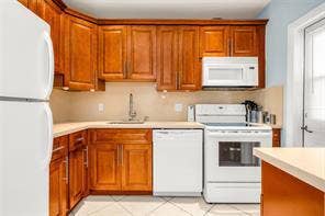 Kitchen featuring wood-finish cabinetry, solid surface countertops, a white appliance suite, and tile flooring