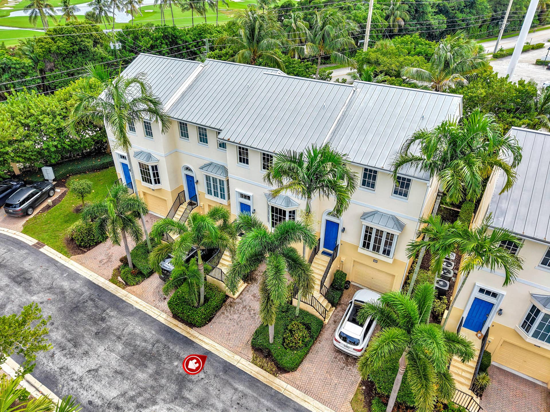 471 JUNO DUNES Way, Juno Beach, FL 33408 Townhome exterior featuring a metal roof, yellow stucco siding, bay windows, and private driveways with paver surfaces