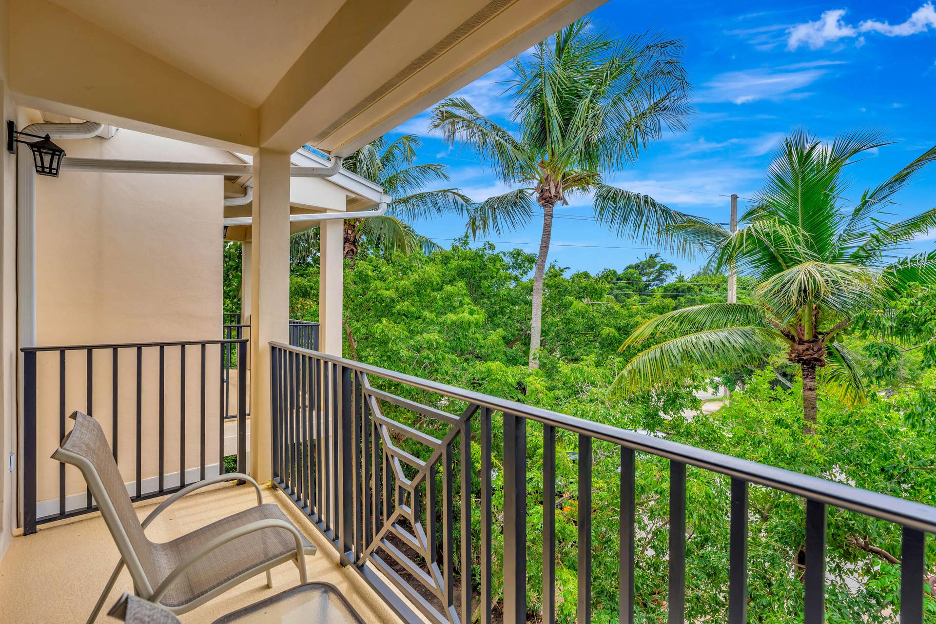 471 JUNO DUNES Way, Juno Beach, FL 33408 Covered balcony with black metal railings, an exterior wall sconce, and a tropical tree canopy
