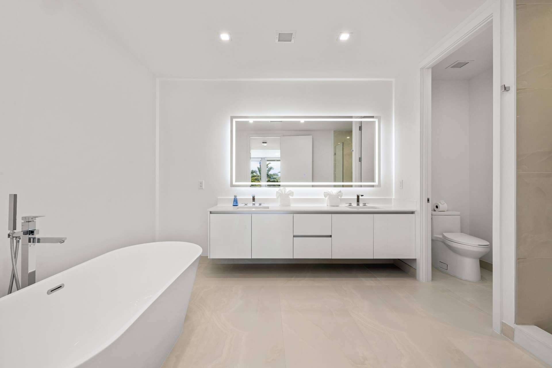 220 Lake Shore Drive, #704, Lake Park, FL 33403 Master Bath - Freestanding soaking tub with floor-mounted chrome faucet, dual vanity with undermount sinks, illuminated mirror, recessed lighting, and large format floor tile