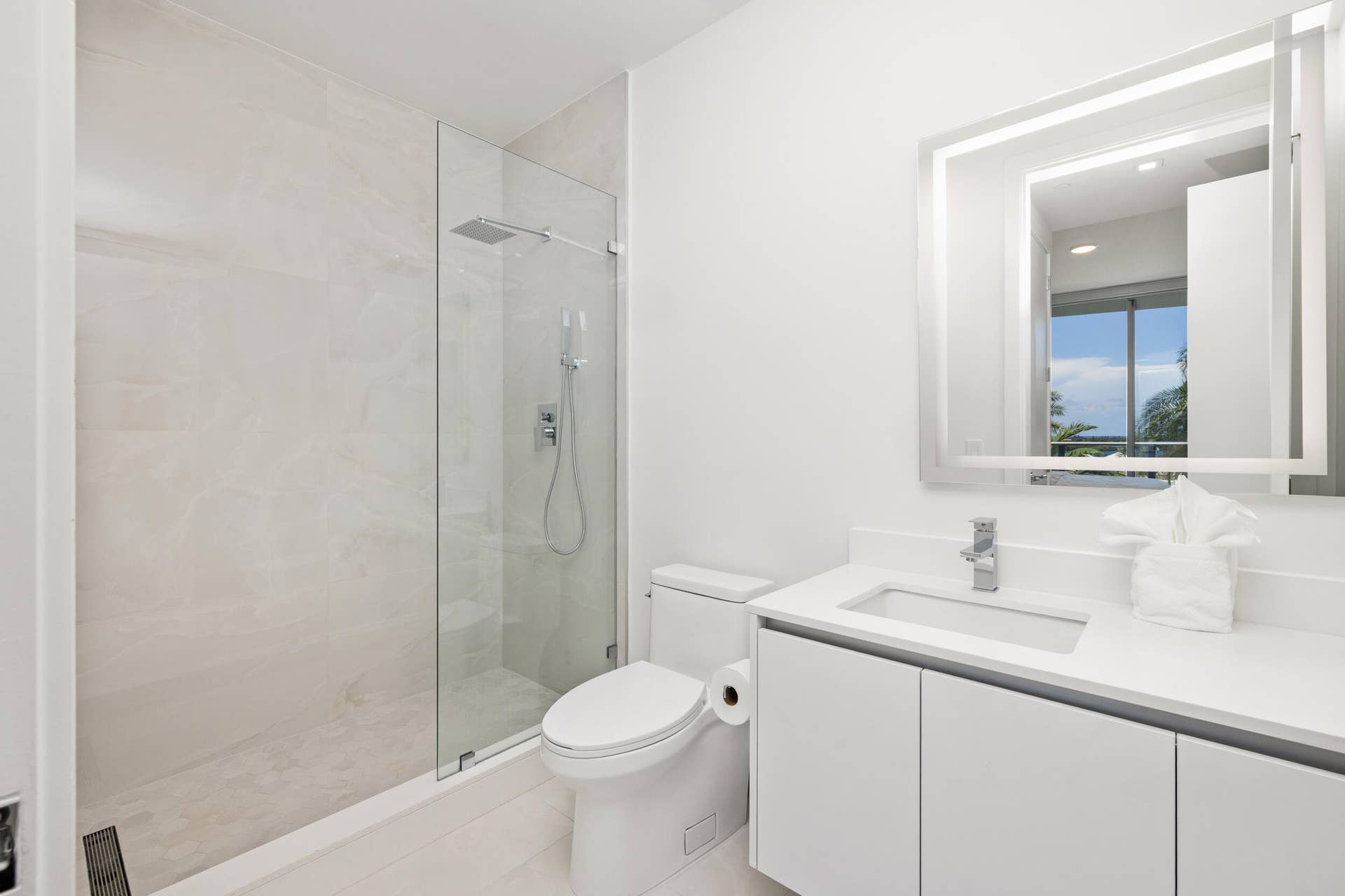 220 Lake Shore Drive, #704, Lake Park, FL 33403 Contemporary bathroom featuring a frameless glass shower, rainfall showerhead, sleek vanity with integrated sink, chrome fixtures, and an illuminated mirror