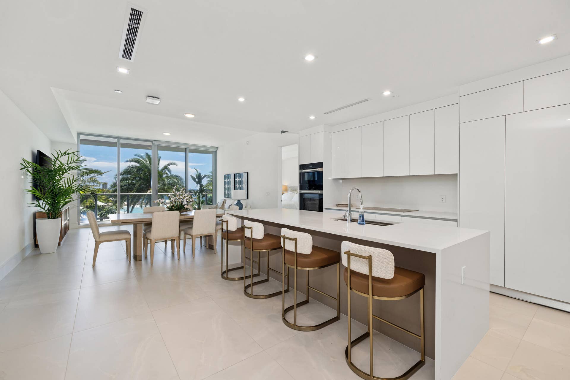 220 Lake Shore Drive, #704, Lake Park, FL 33403 Sleek kitchen with white cabinetry and integrated appliances, expansive central island with countertop seating, open-concept living space, extensive floor-to-ceiling windows, and recessed lighting