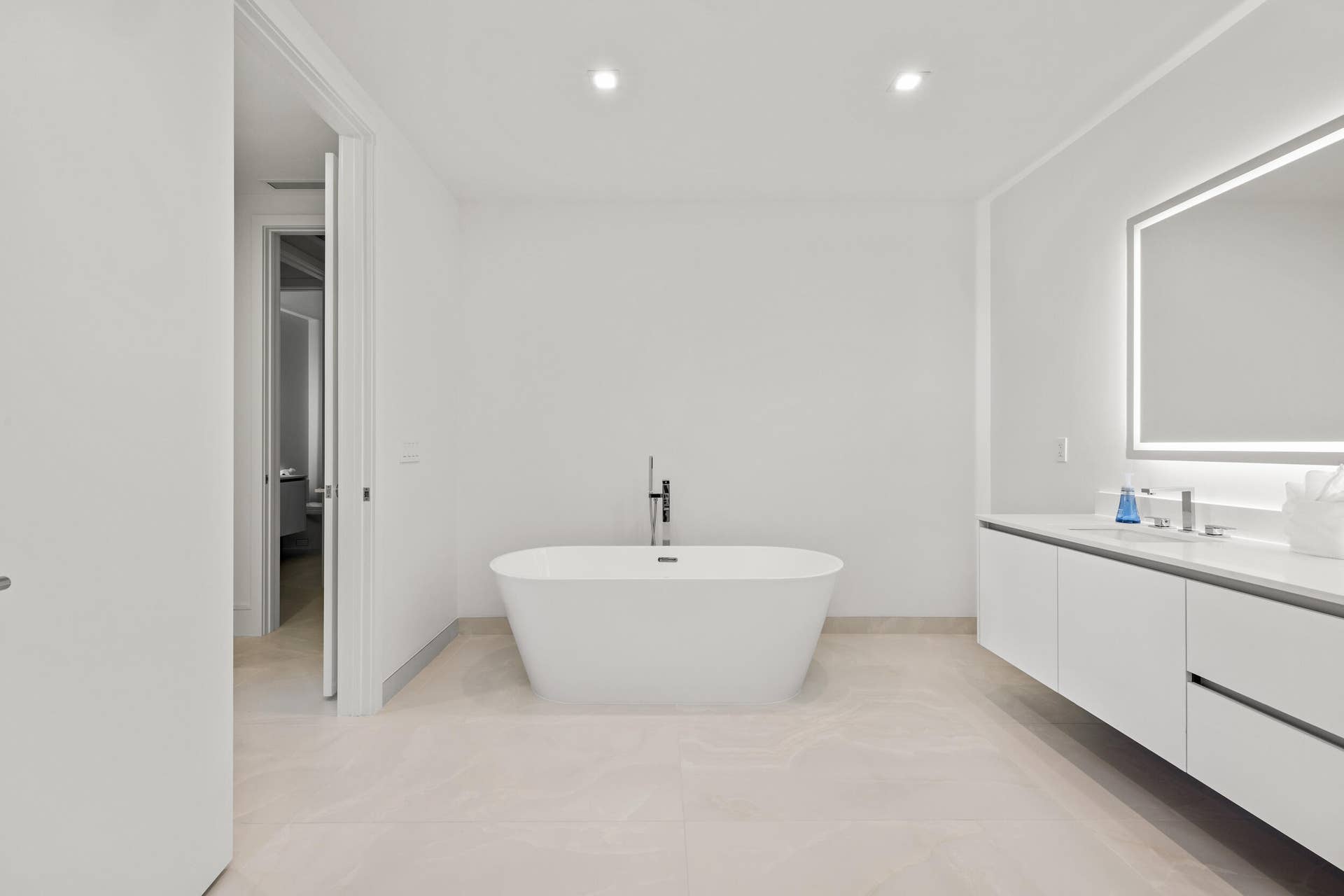 220 Lake Shore Drive, #704, Lake Park, FL 33403 Master Bath - Freestanding soaking tub with floor-mounted faucet, dual-sink floating vanity with white flat-panel cabinetry, light-toned tile flooring, and an illuminated mirror