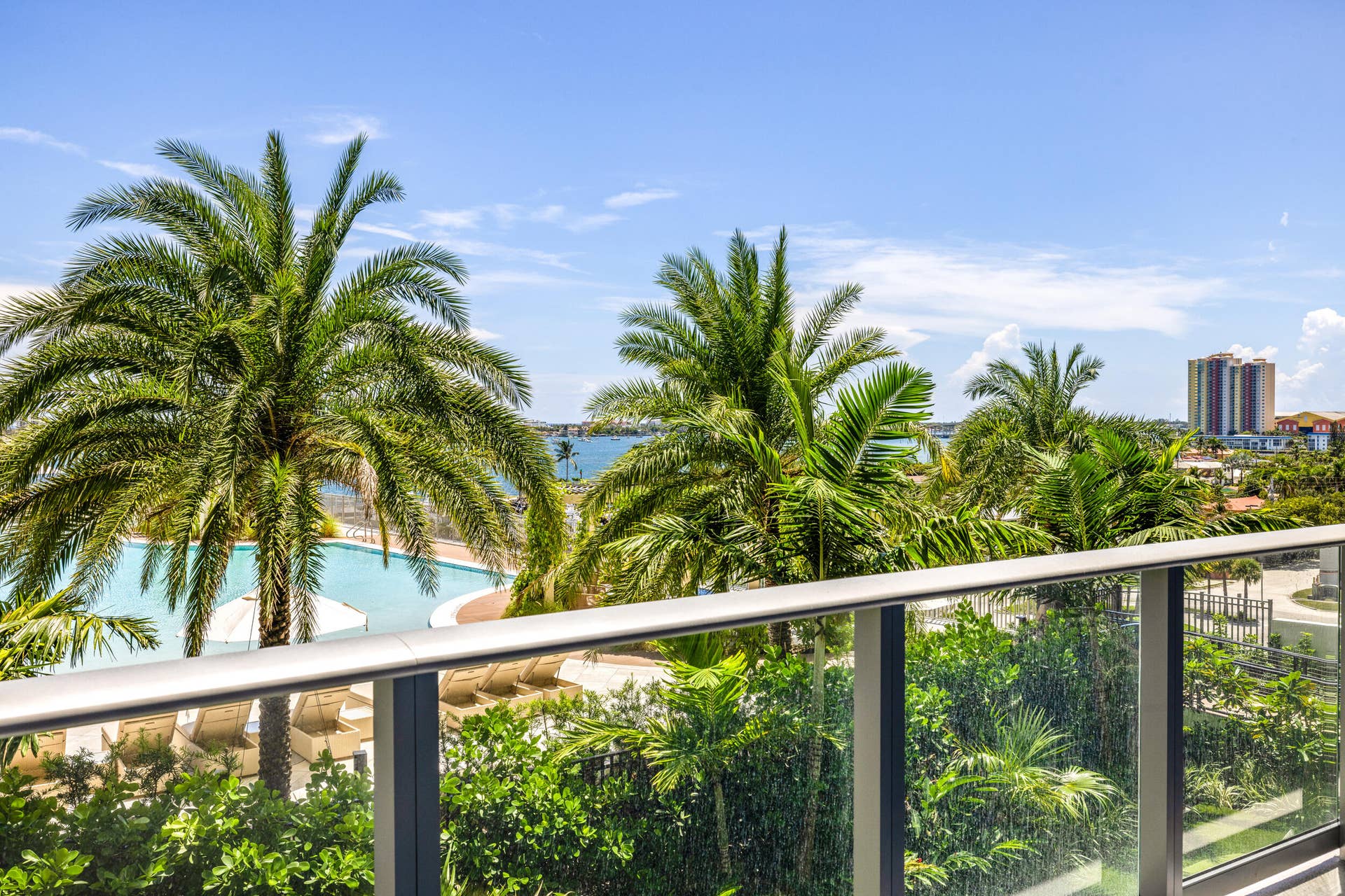 220 Lake Shore Drive, #704, Lake Park, FL 33403 Glass balcony railing with aluminum supports, offering expansive views of tropical landscaping, a resort-style pool, and distant waterways