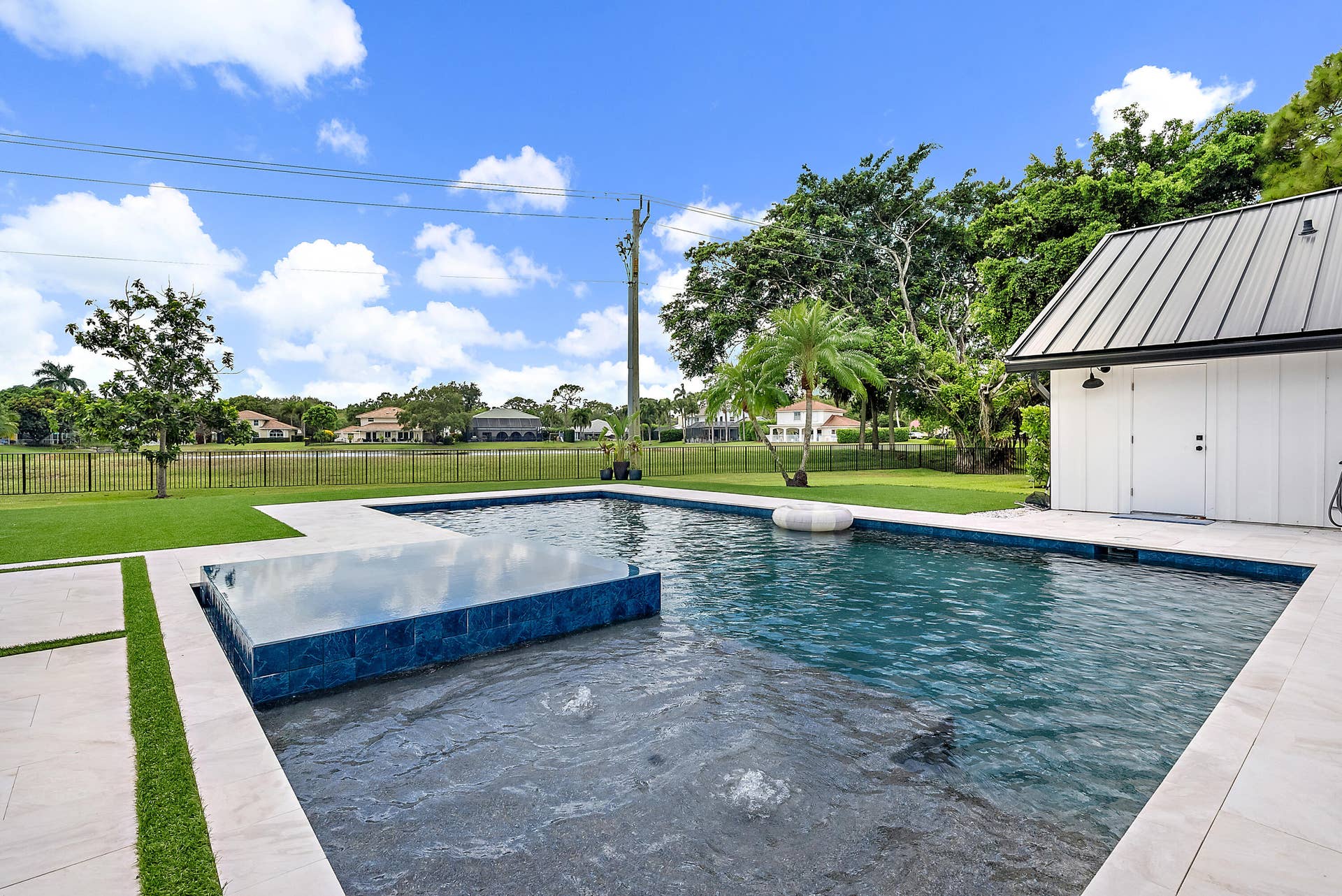 6204 SAND PINE Court, Jupiter, Jupiter, FL 33458 Pool area featuring a tiled water feature, light-toned paver decking, and an adjacent structure with a metal roof