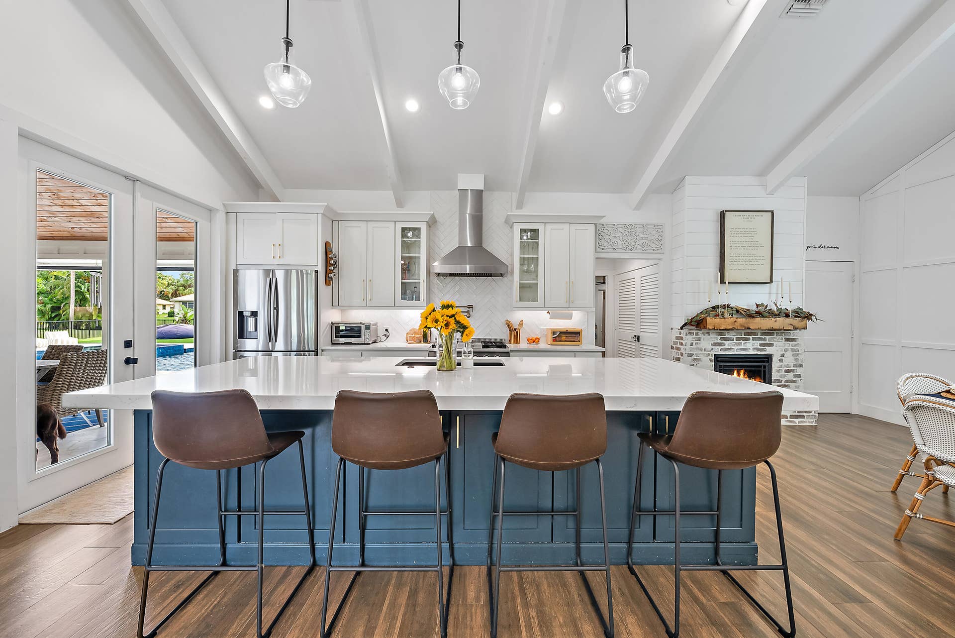 6204 SAND PINE Court, Jupiter, Jupiter, FL 33458 Kitchen featuring a large island with white countertop, stainless steel appliances, exposed ceiling beams, and a fireplace with a brick surround