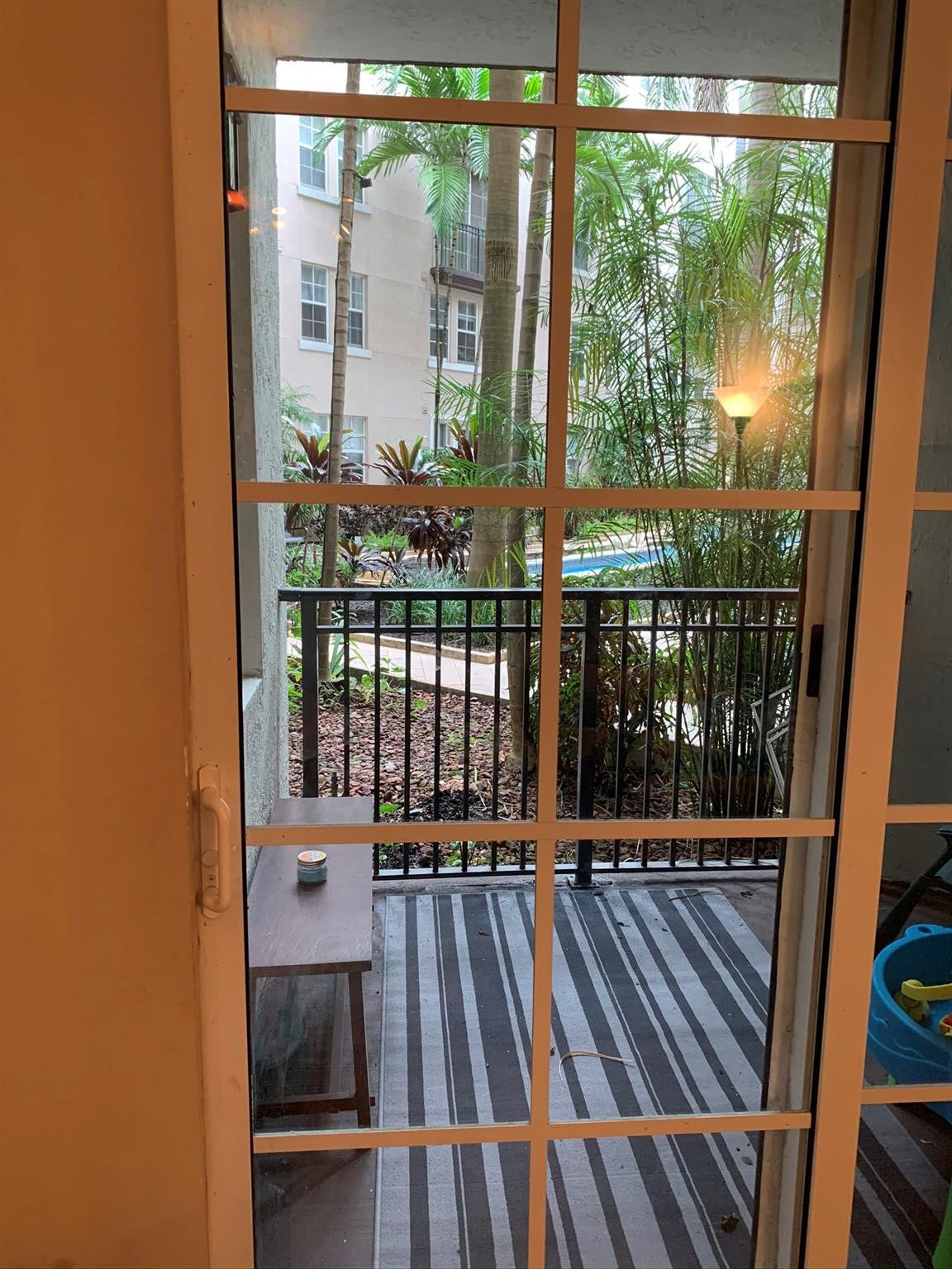533 NE 3RD Avenue, #115, Fort Lauderdale, Fort Lauderdale, FL 33301 French doors with wood-frame muntins open to a striped composite deck with black metal railings and lush landscaping featuring mature trees and tropical plantings visible beyond the property perimeter