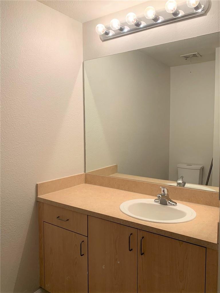 533 NE 3RD Avenue, #115, Fort Lauderdale, Fort Lauderdale, FL 33301 Bathroom vanity featuring warm wood-finish cabinetry with ample storage, a solid countertop with integrated round sink, chrome faucet fixture, and illuminated mirror with Hollywood-style vanity lighting