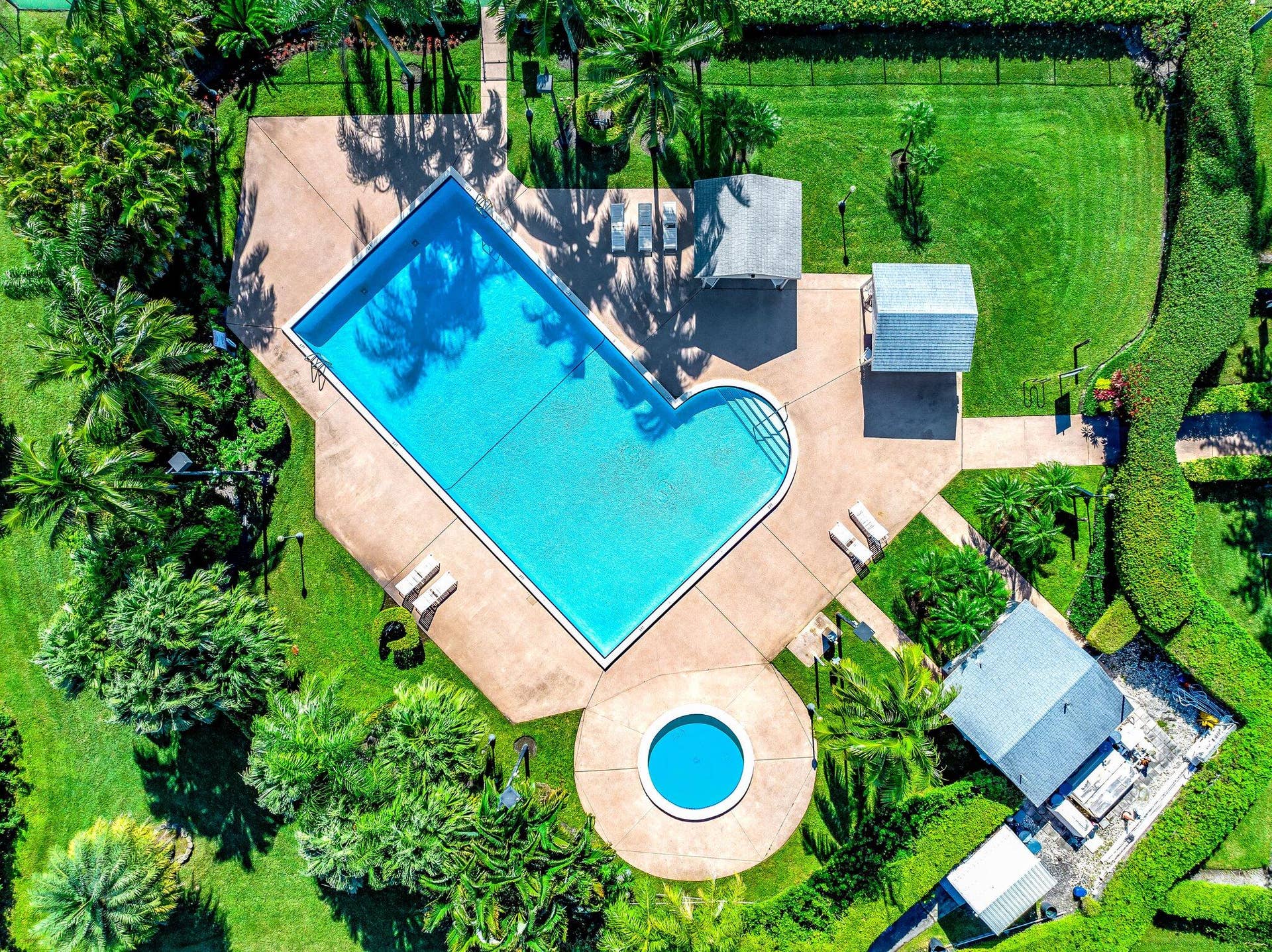 Expansive outdoor area featuring a swimming pool, circular spa, surrounding concrete patio, and lush landscaping