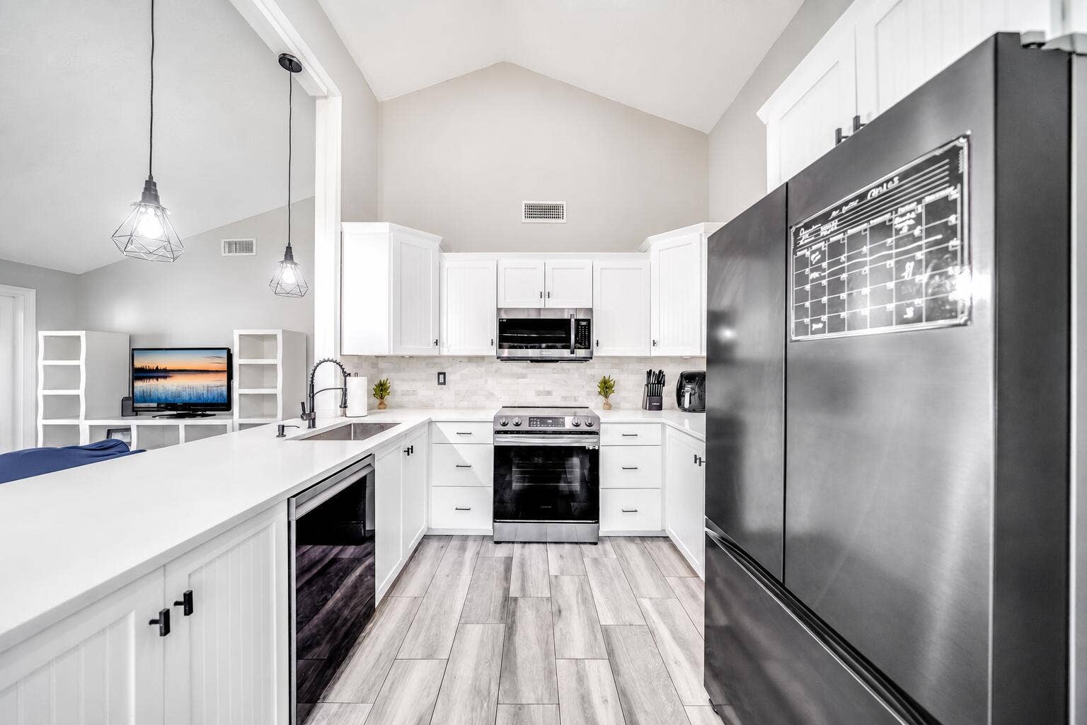 Kitchen featuring vaulted ceilings, white cabinetry, stainless steel appliances, wood-finish flooring, and a white countertop