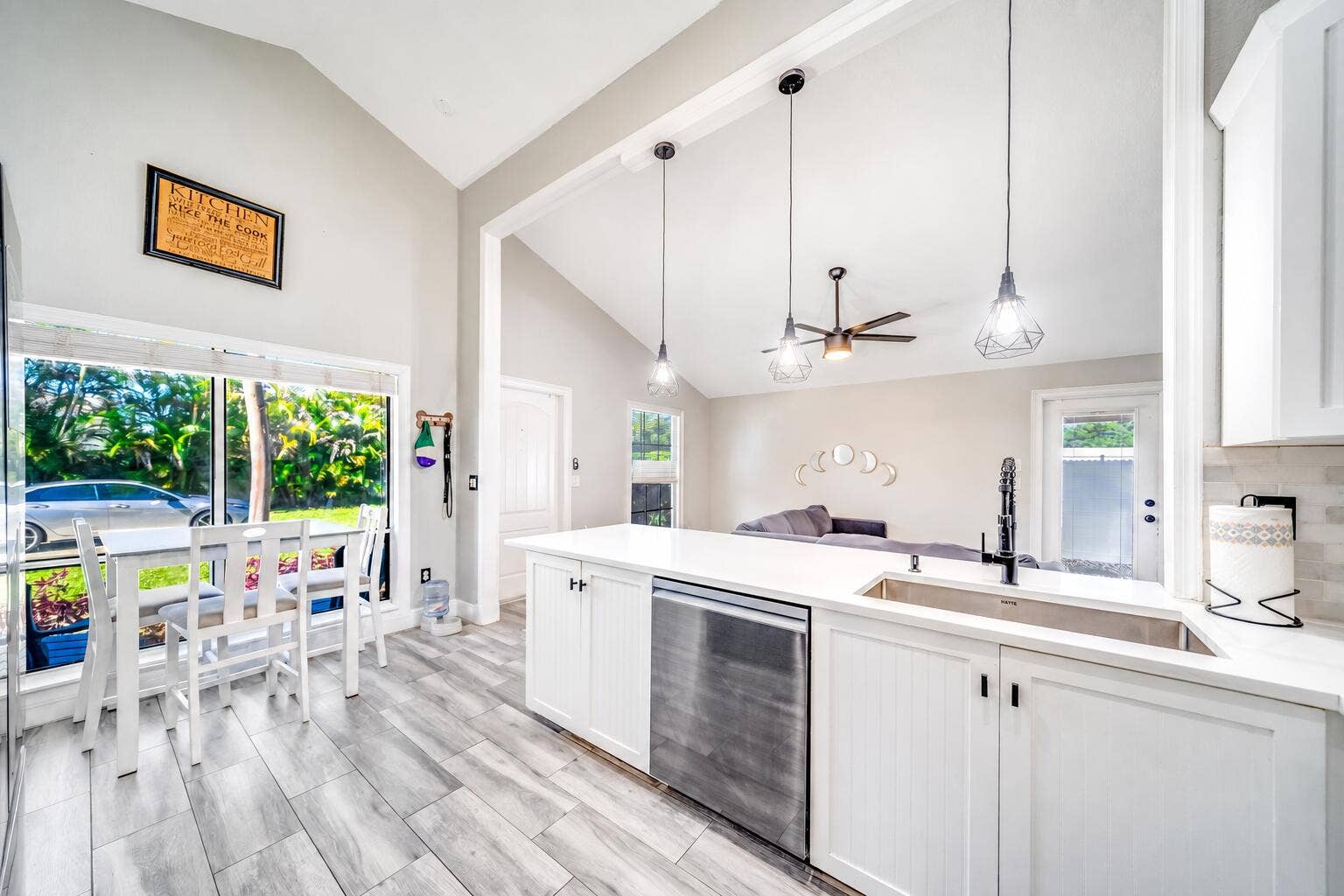 Vaulted ceilings, wood-finish flooring, white cabinetry, stainless steel dishwasher, and a stainless steel sink with a black gooseneck faucet