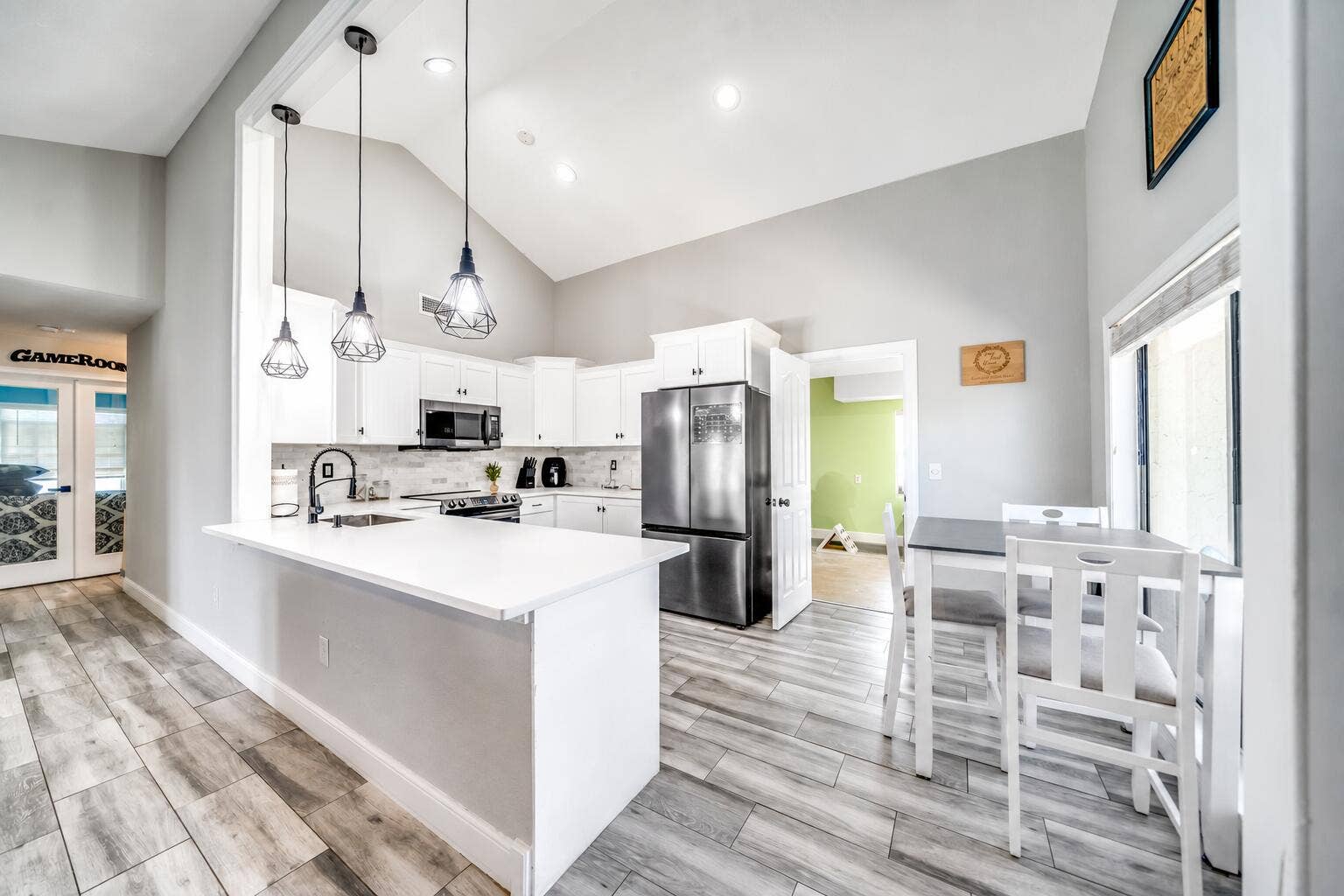 Kitchen featuring vaulted ceilings, wood-finish flooring, white cabinetry, stainless steel appliances, and a kitchen island with pendant lighting
