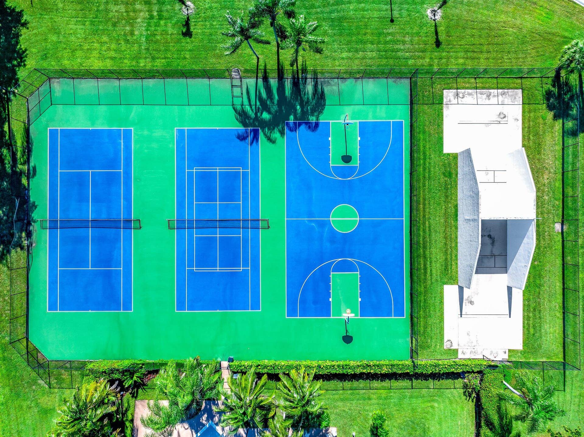 Expansive recreational area featuring two blue tennis courts, a full-sized basketball court, and a multi-purpose concrete structure