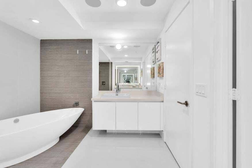 Sunny Isles Beach, Sunny Isles Beach, FL 33160 Freestanding soaking tub with a tiled accent wall, single vanity with integrated sink, and large mirror with integrated lighting