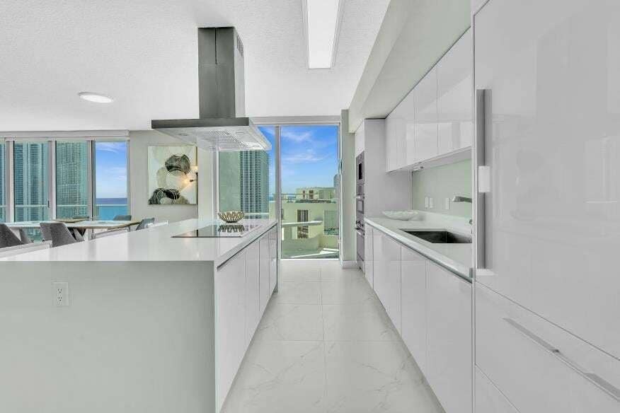 Sunny Isles Beach, Sunny Isles Beach, FL 33160 Sleek kitchen featuring an oversized island, integrated cooktop, stainless steel range hood, wall ovens, and custom white cabinetry