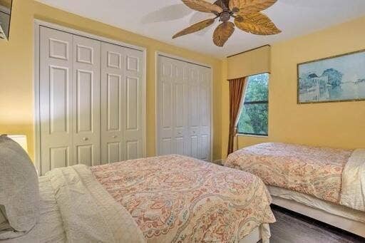 Wood-finish flooring, two sets of bi-fold closet doors, ceiling fan with leaf-shaped blades, and window with solid valance