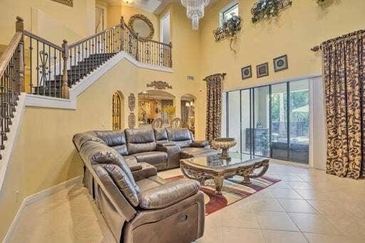 Two-story ceiling, grand staircase with wrought iron balusters, tile flooring, and sliding glass doors