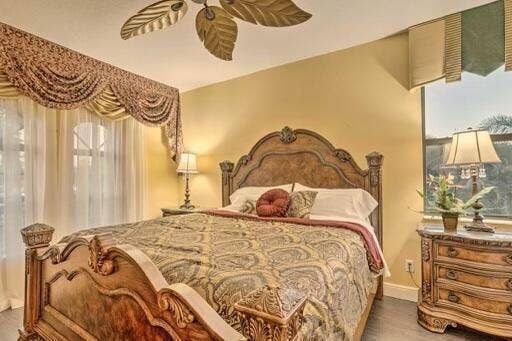 Ceiling fan with leaf-shaped blades, decorative window treatments, wood-finish flooring, and a large window