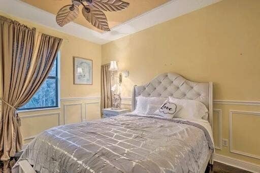 Tray ceiling with a decorative fan, window with trim, decorative wainscoting, and a tufted headboard