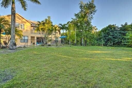 Expansive green lawn with a perimeter fence, tropical landscaping, and mature trees