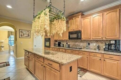 Kitchen featuring an expansive island with a granite countertop, light wood-finish cabinetry, built-in microwave, and tile flooring