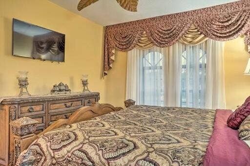 Wall-mounted display, decorative wall sconces, wood-finish dresser with carved details, arched windows, and ornamental valance