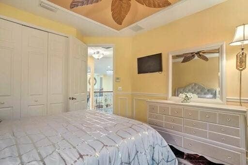 Recessed panel closet doors, decorative ceiling fan, wall-mounted television, wainscoting, and a large wall mirror