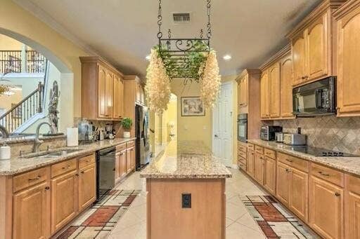 Kitchen featuring light wood cabinetry, granite countertops, a central island, and a built-in oven and microwave
