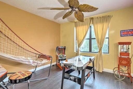 Room featuring wood-finish flooring, a ceiling fan with leaf-shaped blades, and windows with neutral-toned drapes