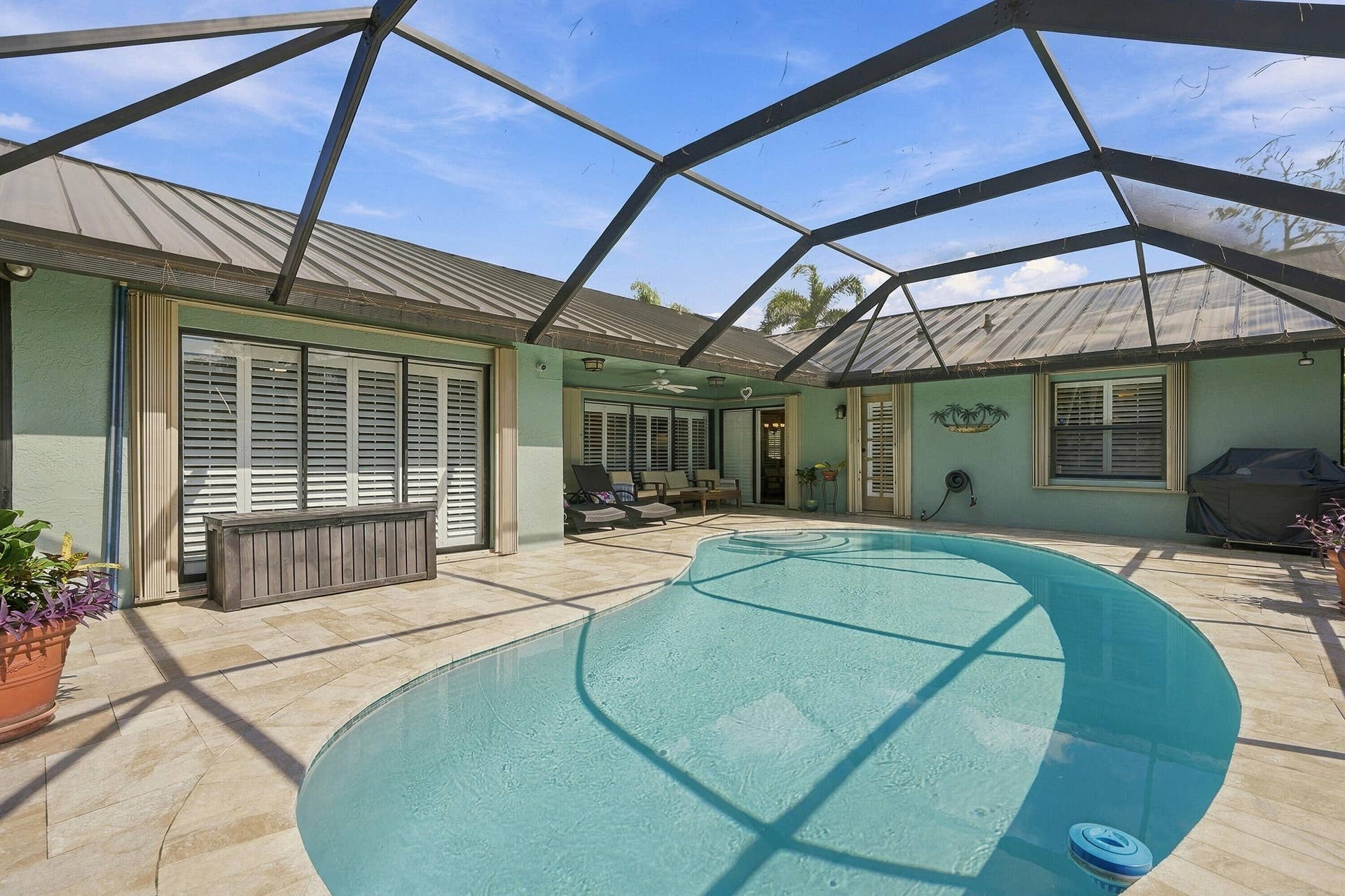 Screen-enclosed pool area featuring a freeform swimming pool, extensive paved patio, and a covered lanai