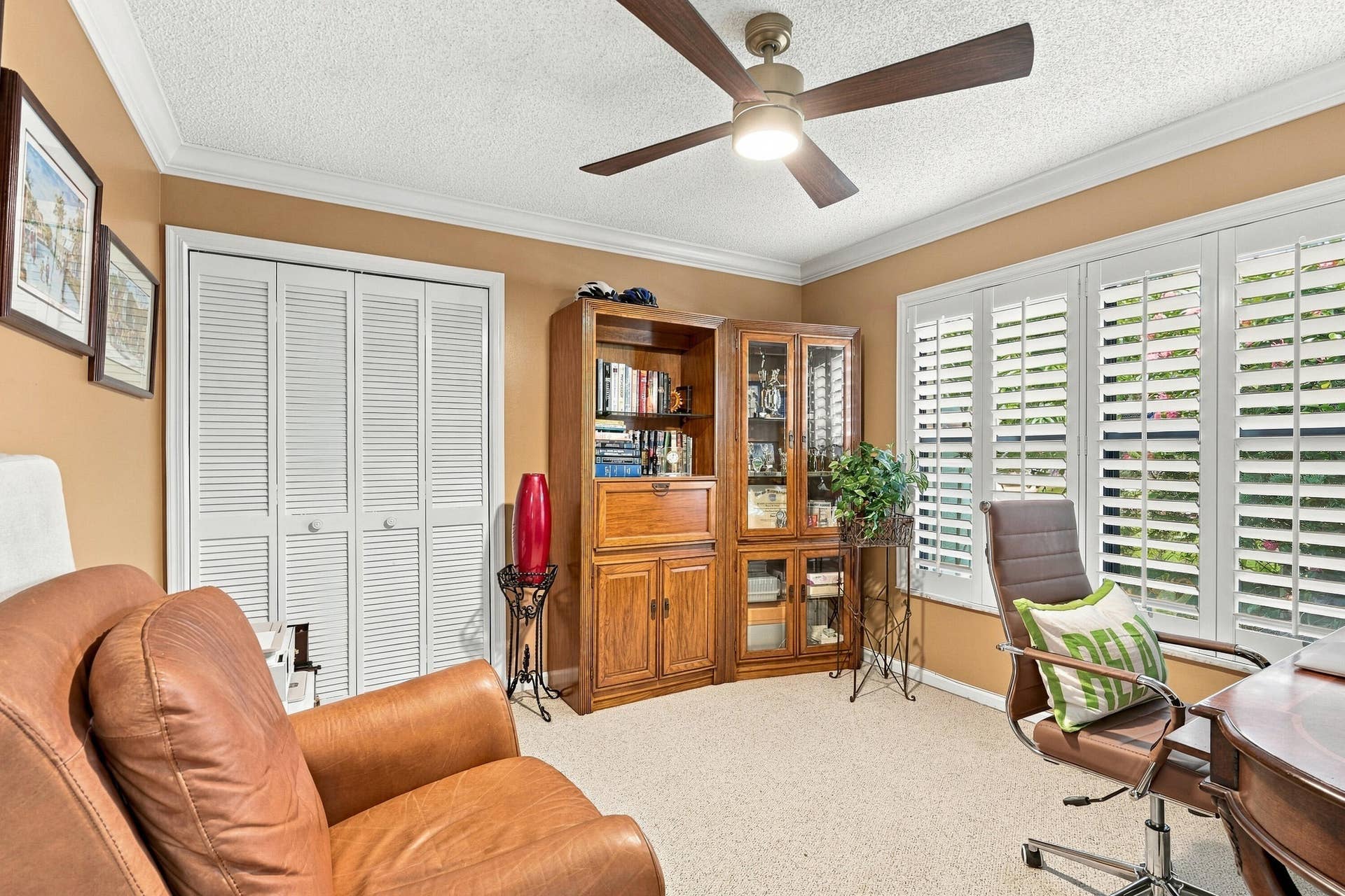 White louvered bi-fold closet doors, crown molding, ceiling fan with integrated lighting, wood-finish built-in cabinetry, and white plantation shutters