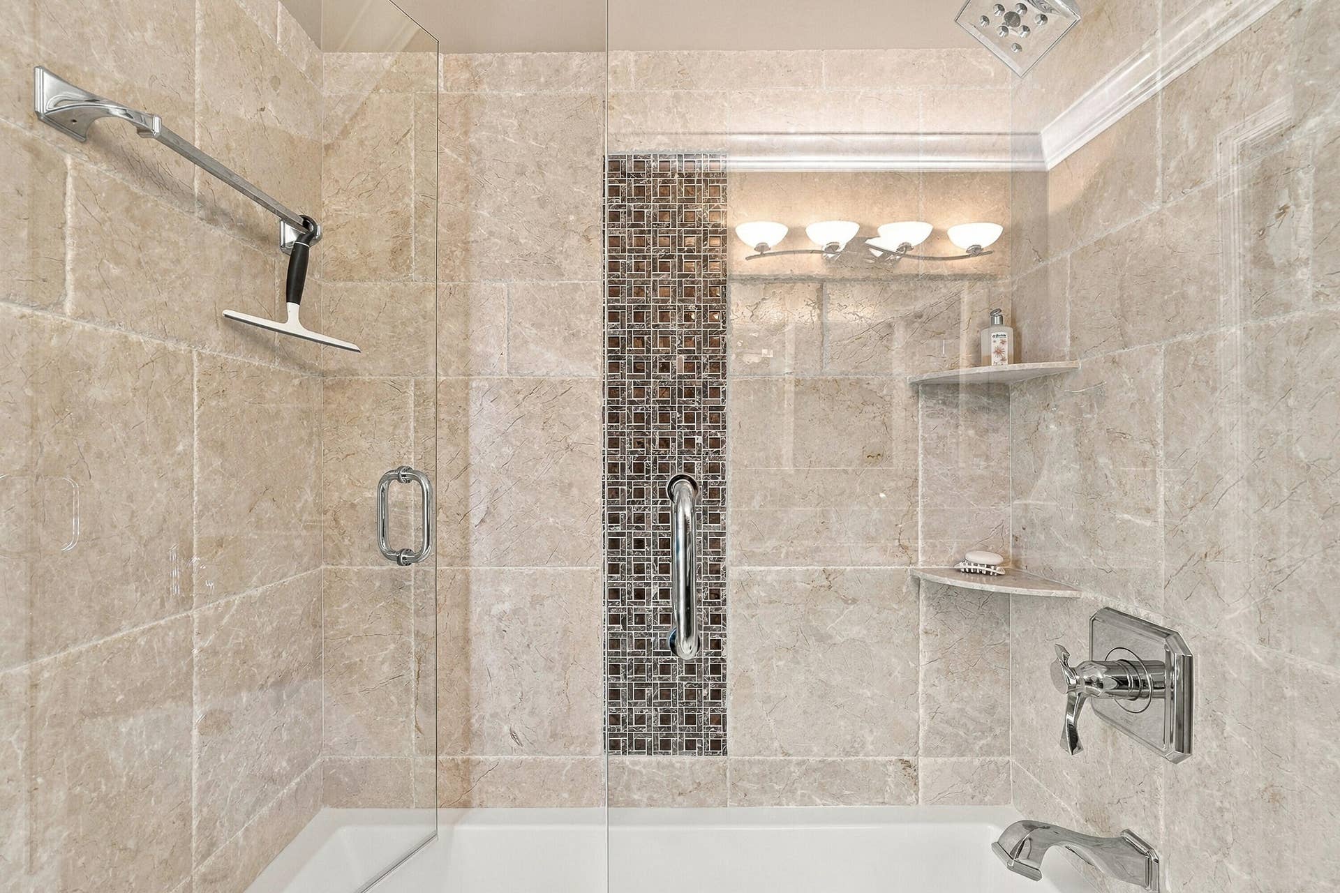 Tiled shower featuring a glass enclosure, decorative mosaic tile accent, built-in shelving, and a chrome shower head with a separate handheld spray