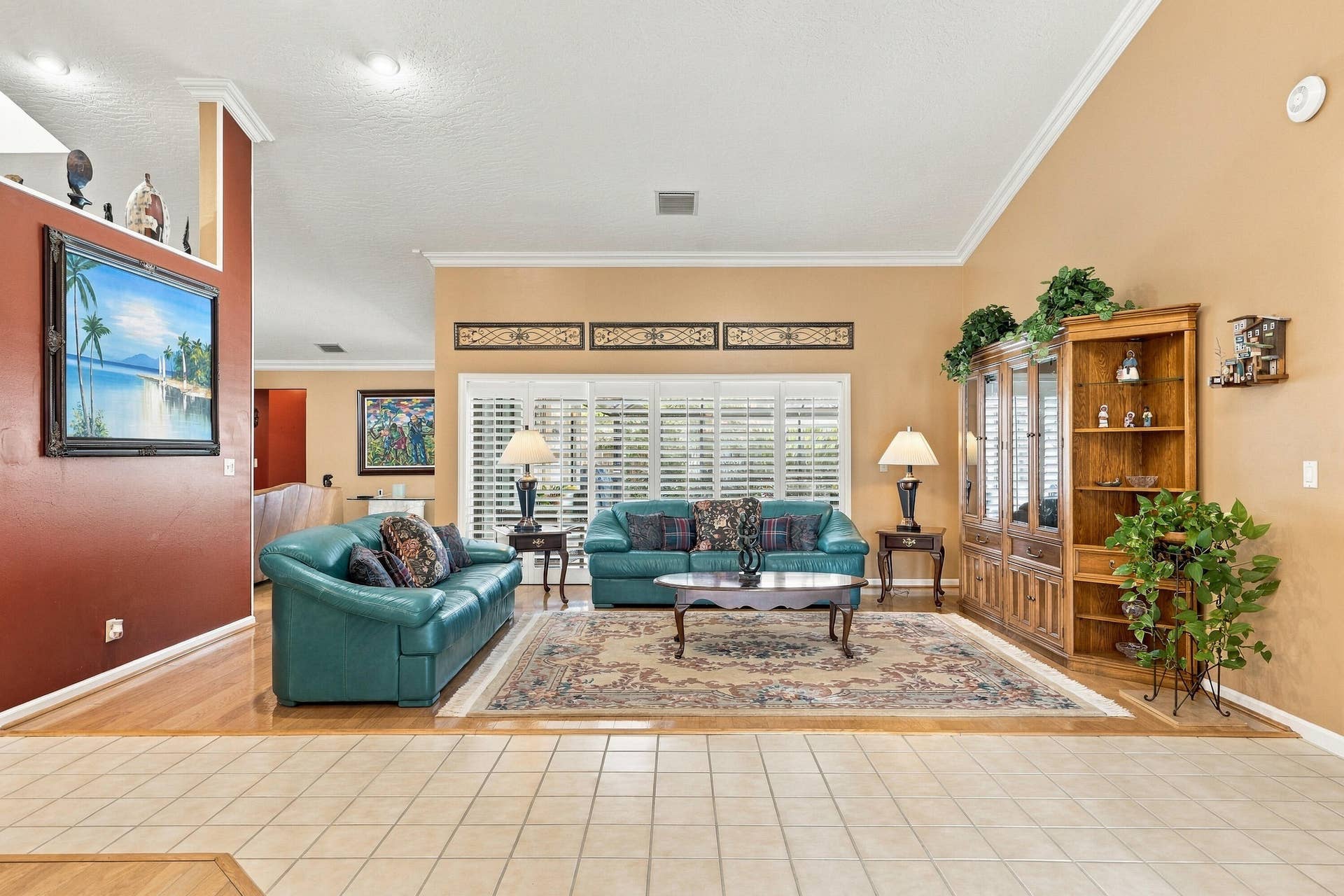 Spacious living area featuring vaulted ceilings, crown molding, a built-in display cabinet, and plantation shutters