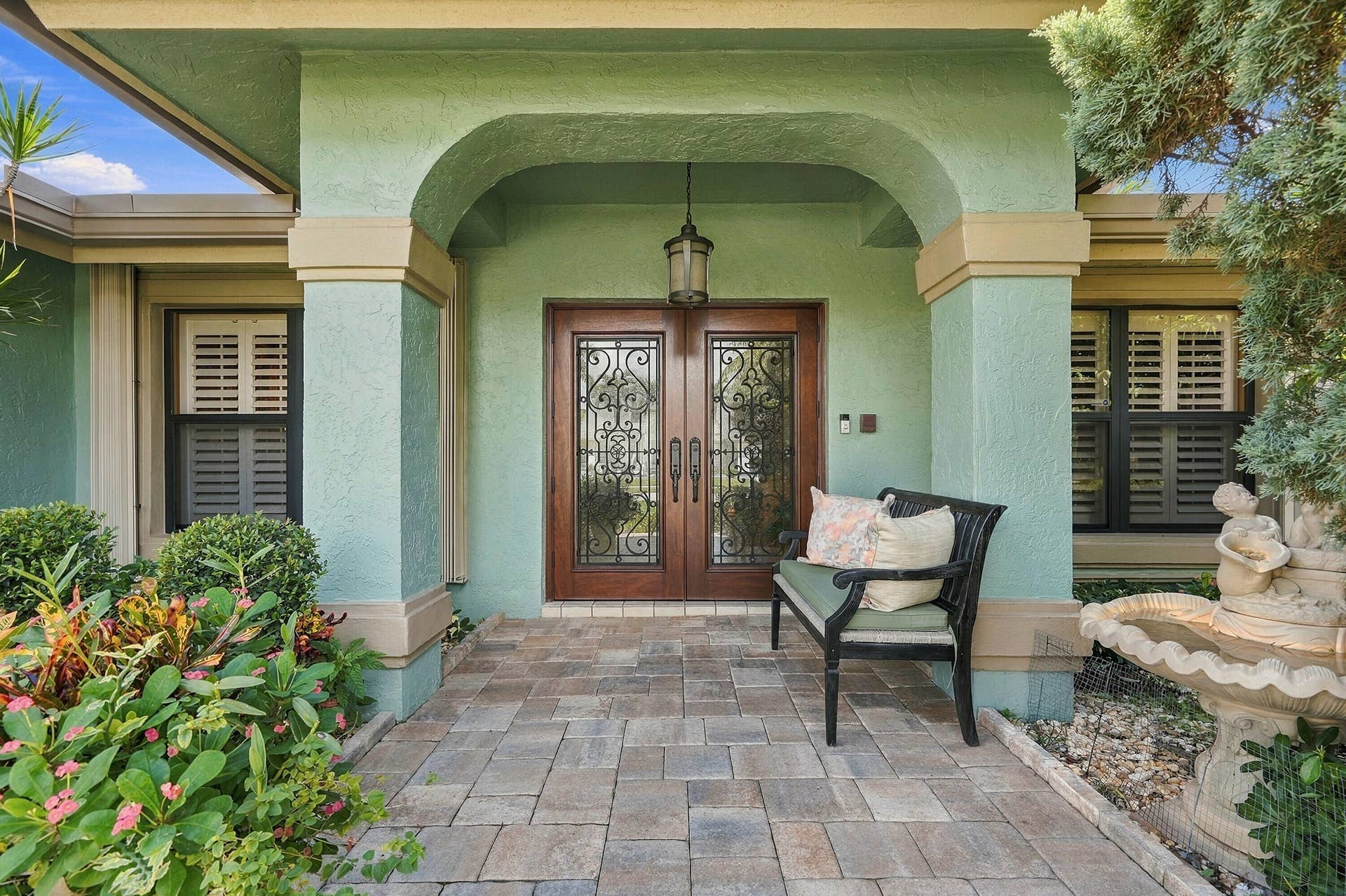 Paver walkway leading to an arched entry with a decorative double-door entry, exterior lighting, and built-in window shutters