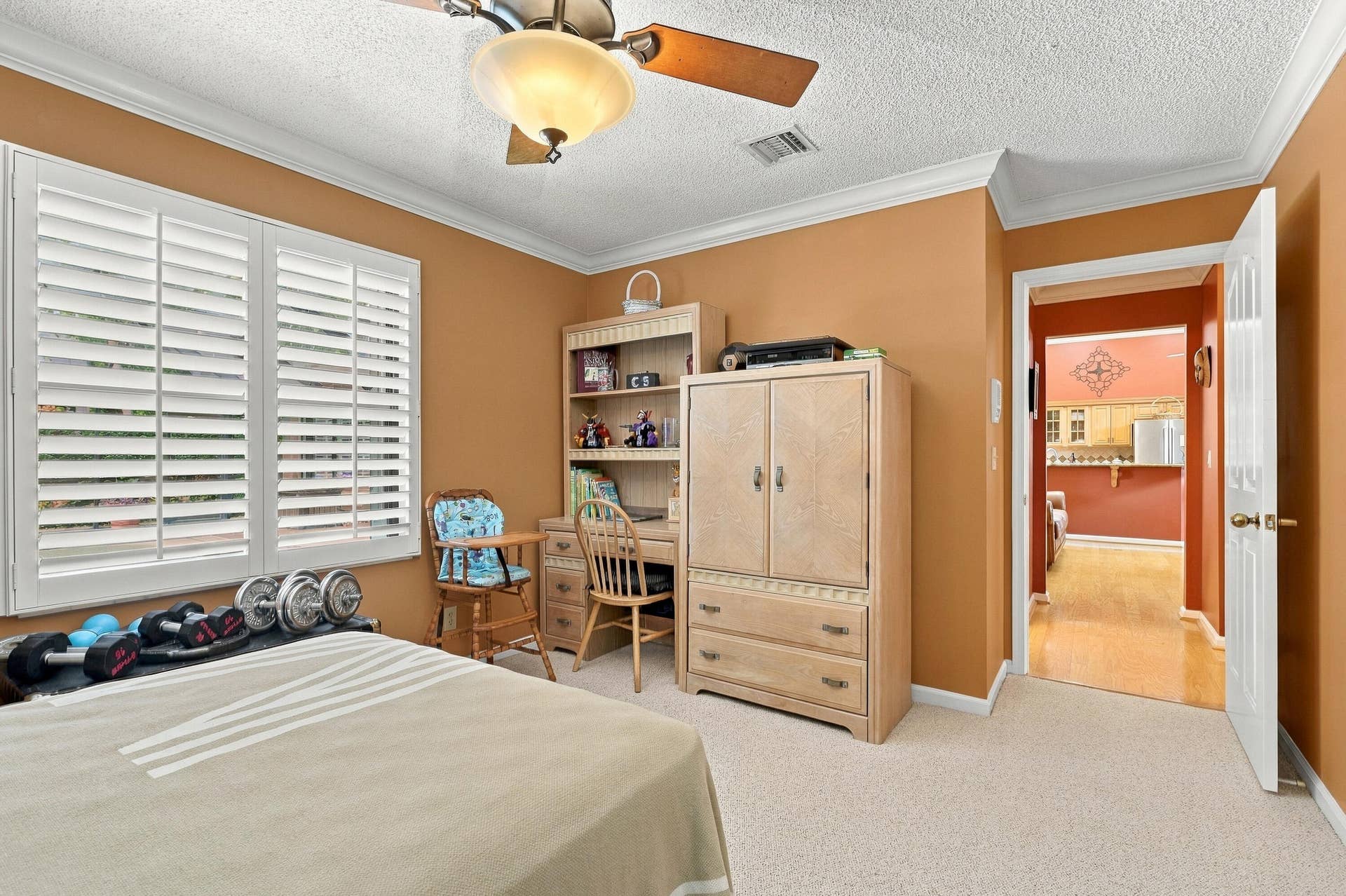 Crown molding, ceiling fan with integrated lighting, window with plantation shutters, and light-colored carpeting