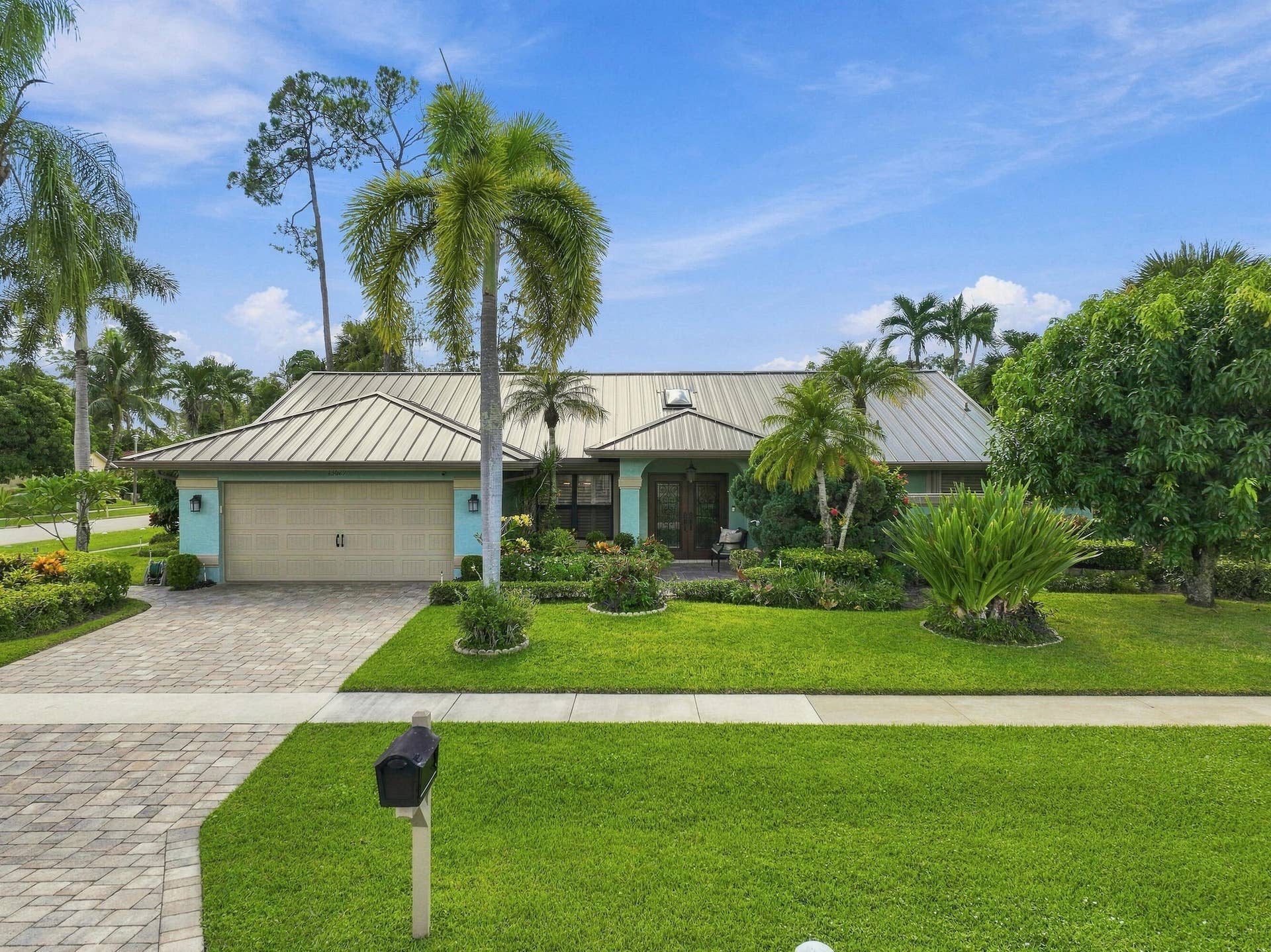 Metal roof, light blue exterior, attached garage, paver driveway, and mature landscaping