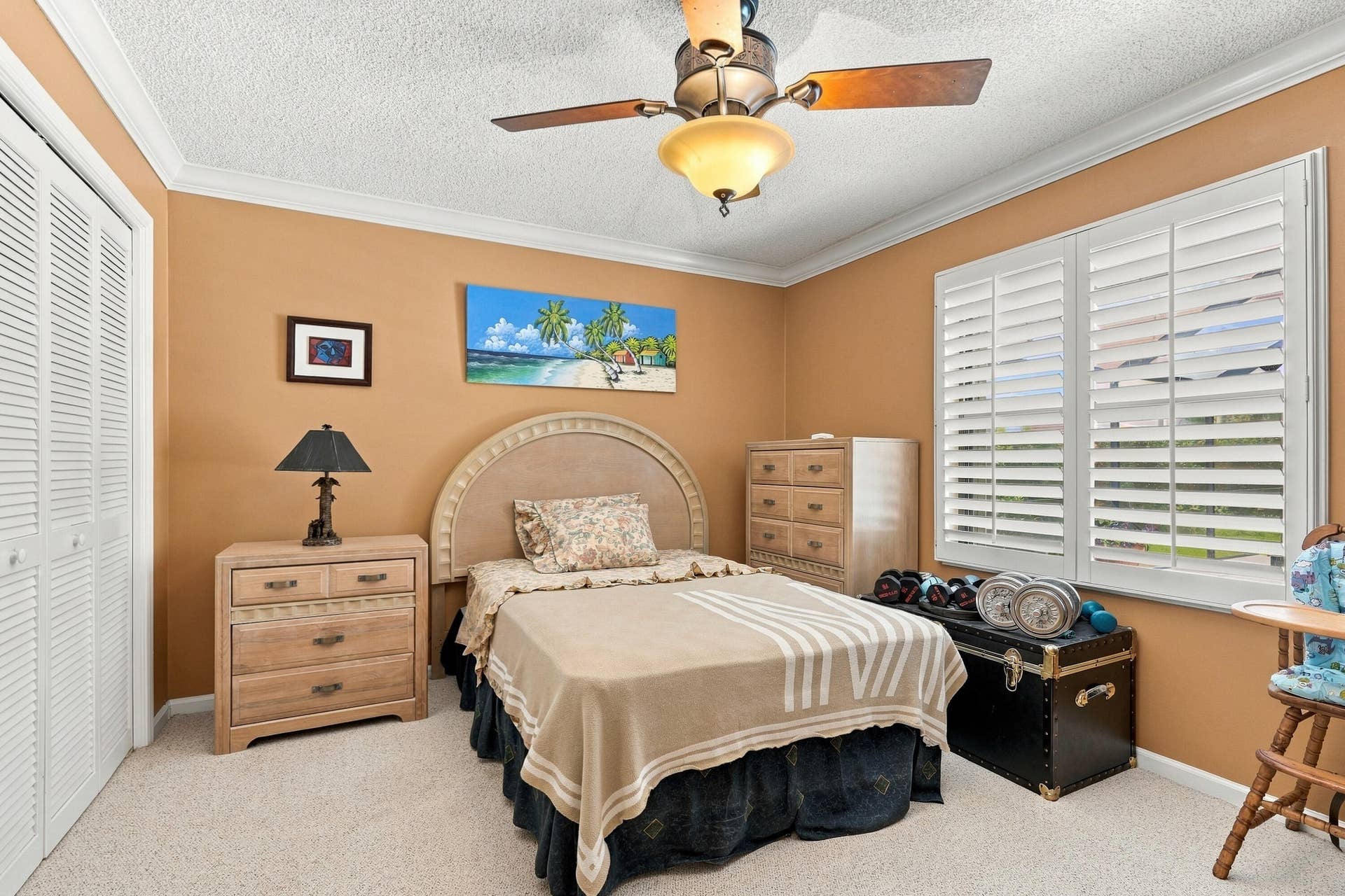 Louvered bi-fold closet doors, crown molding, ceiling fan with integrated lighting, window with white plantation shutters, and carpeted flooring