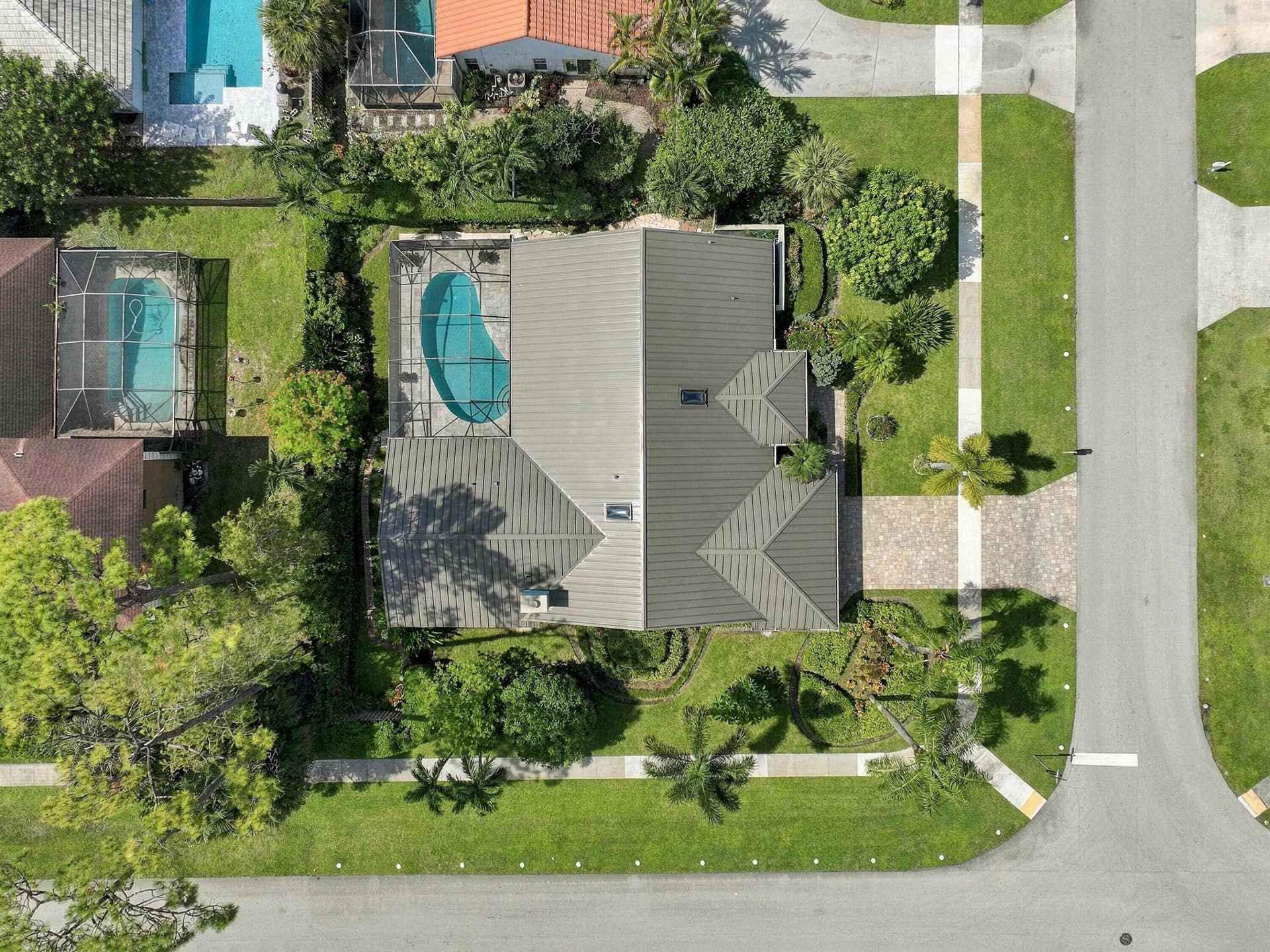 Pitched roof design, screened-in swimming pool, paver driveway, manicured lawn, and mature landscaping
