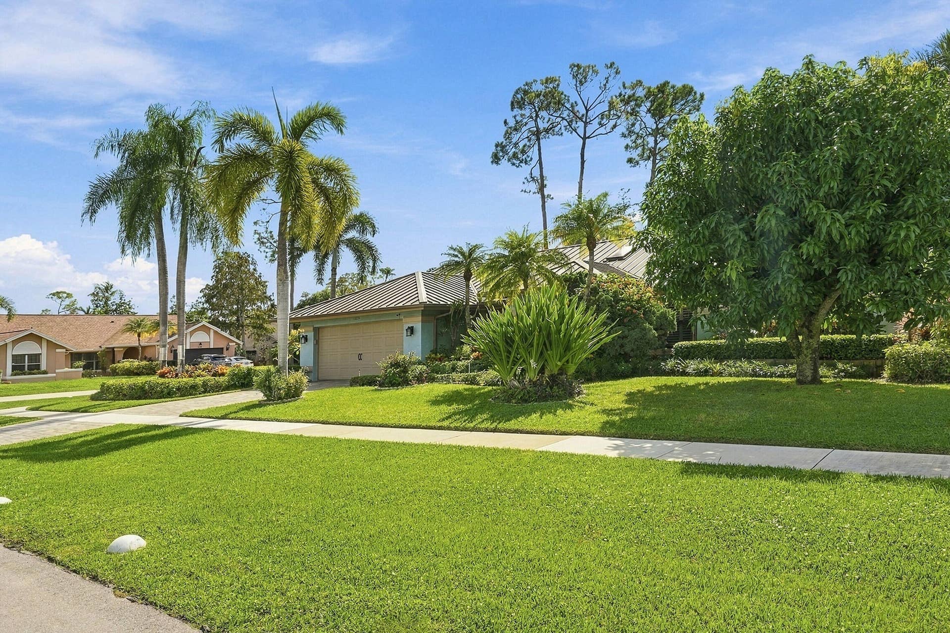 Manicured front yard with mature landscaping and palm trees, featuring a concrete driveway and sidewalk, and a two-car garage