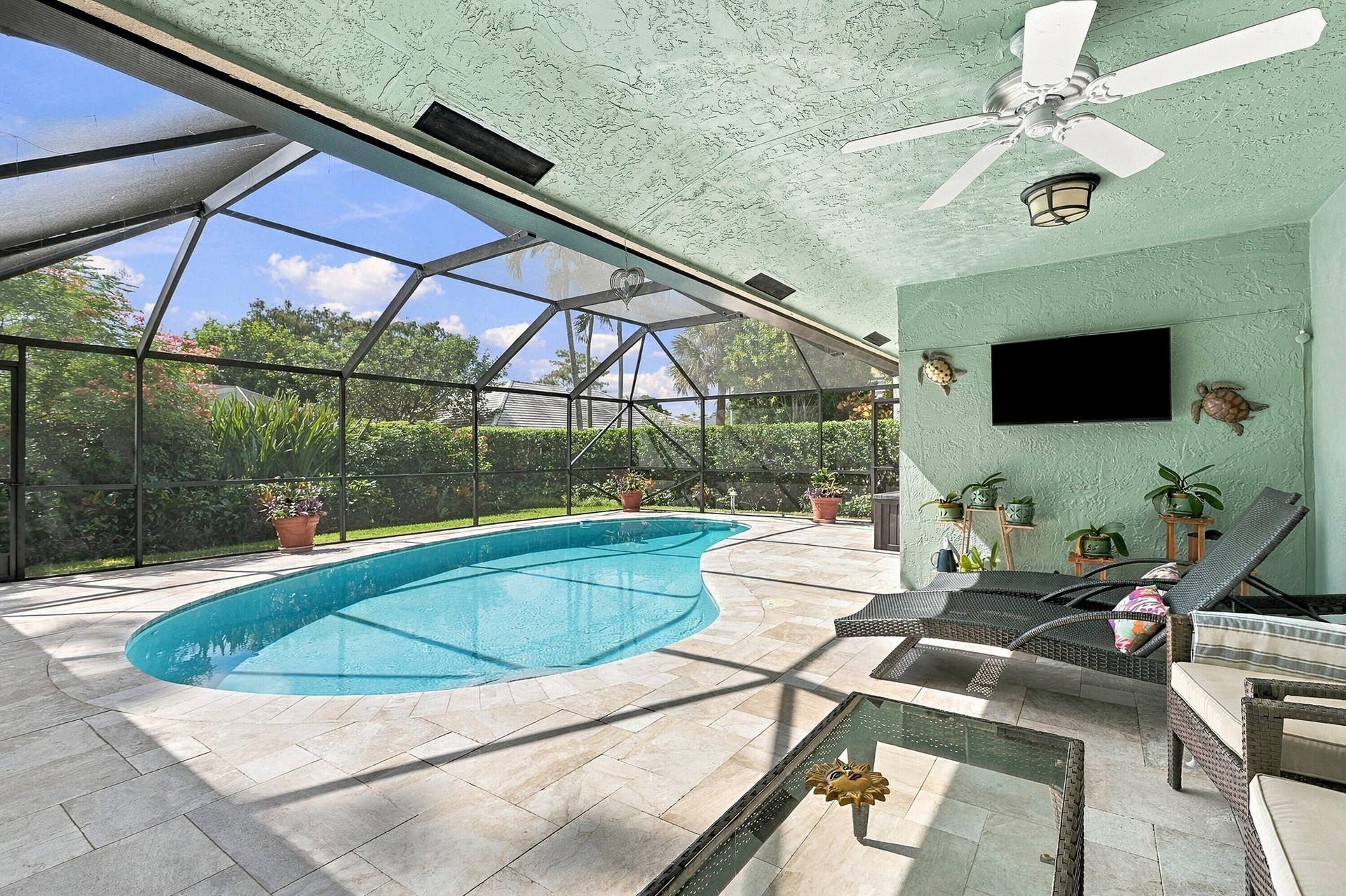 Screened-in pool deck featuring a freeform pool, tiled surround, and textured ceiling with a ceiling fan