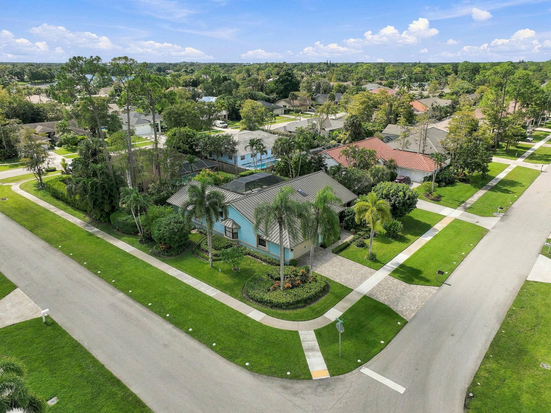 Corner lot home featuring a paver driveway, mature landscaping, and a blue-tiled roof