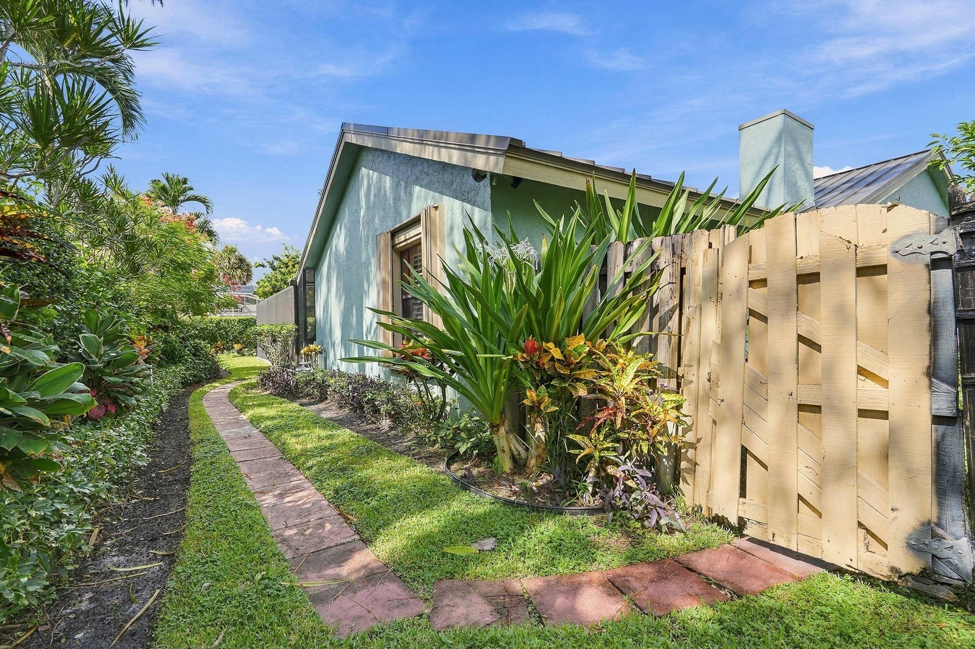 Side yard with a stone pathway, lush landscaping, and a wooden privacy fence