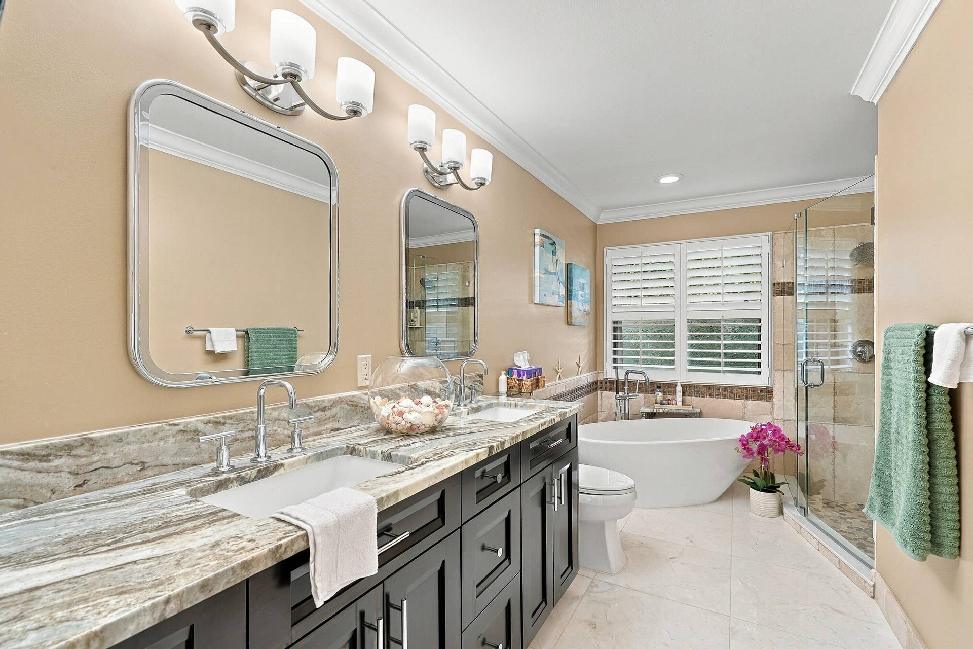 Dual vanity with stone countertop and undermount sinks, contemporary light fixtures, framed mirrors, freestanding soaking tub, and glass-enclosed shower