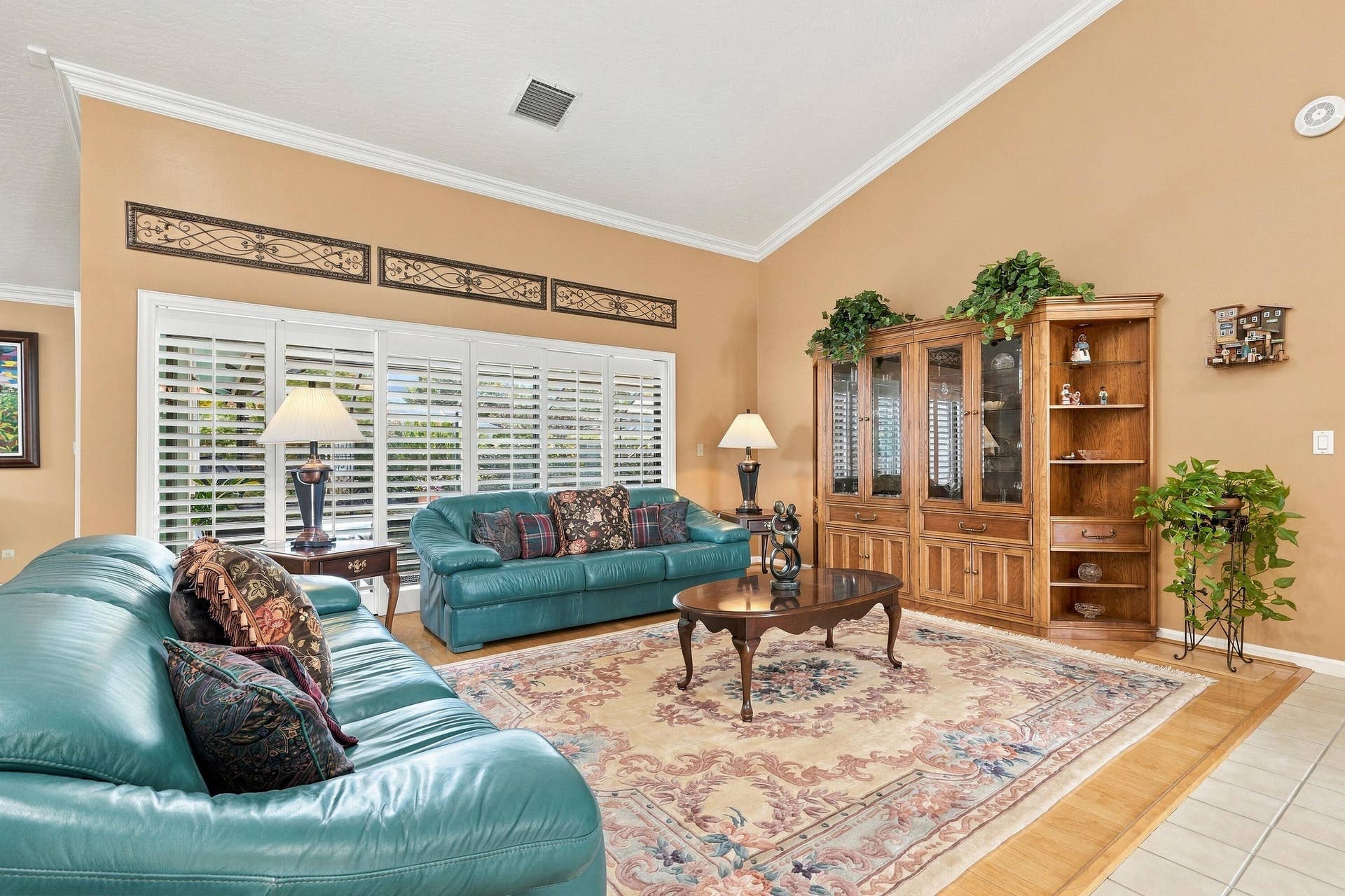 Vaulted ceiling featuring crown molding, large window with plantation shutters, built-in display cabinetry, wood-look flooring, and tile flooring