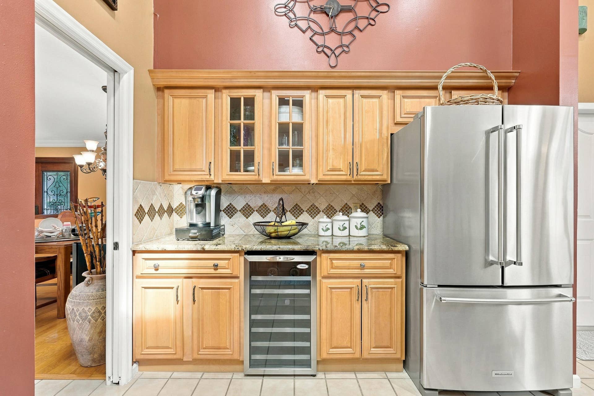 Built-in stainless steel refrigerator, wood-finish cabinetry, patterned tile backsplash, beverage cooler, and stone countertop