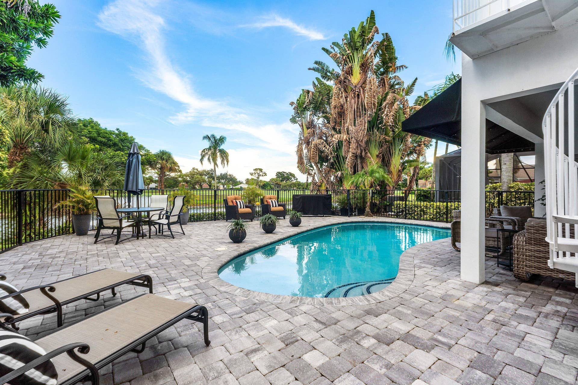 13138 Touchstone Place, Palm Beach Gardens, FL 33418 Curved swimming pool with paver decking, black metal fence, and a spiral staircase