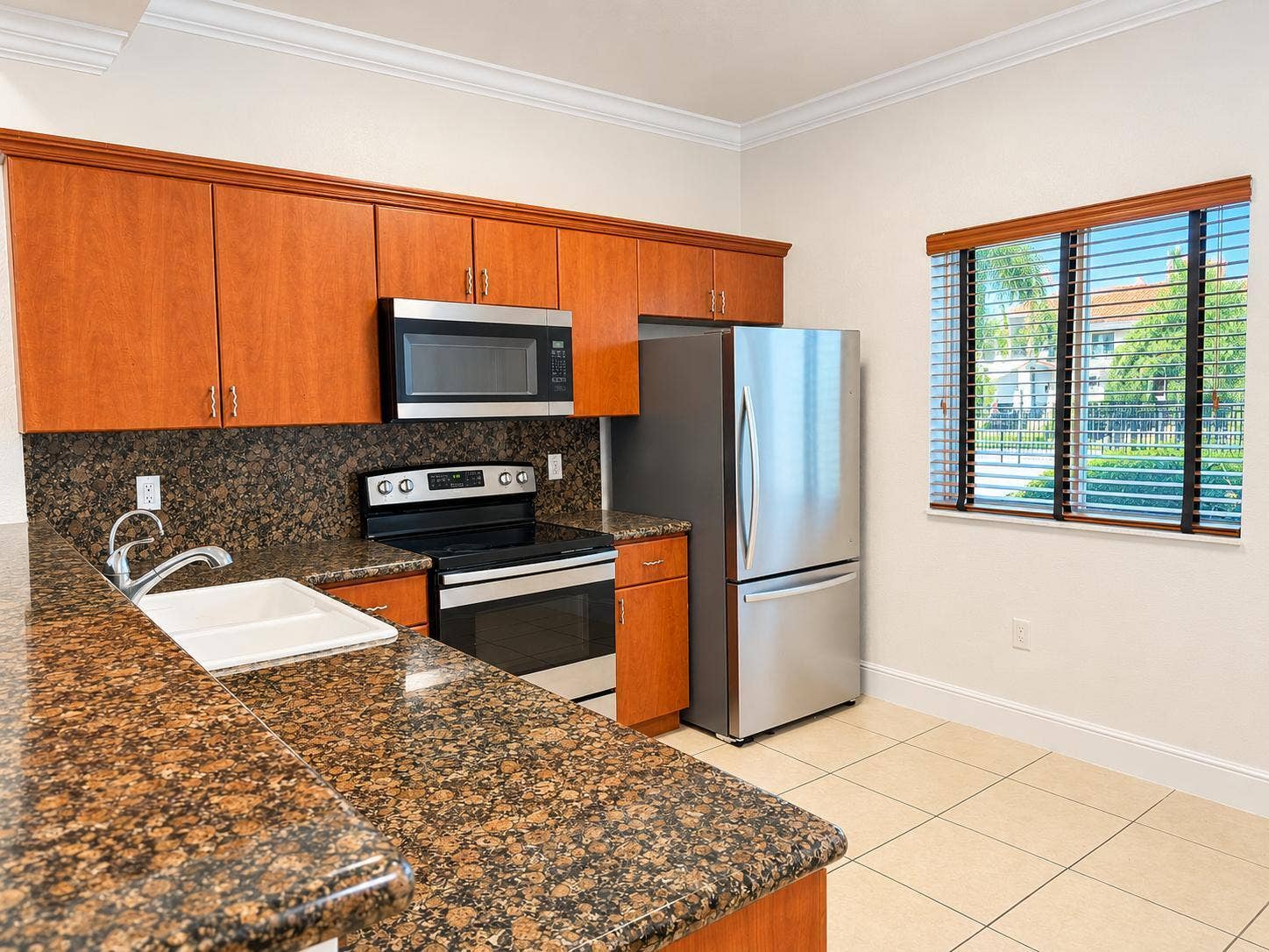 Kitchen featuring wood cabinetry, stone countertops, stainless steel appliances, a stainless steel sink, and tile flooring. Virtually staged.