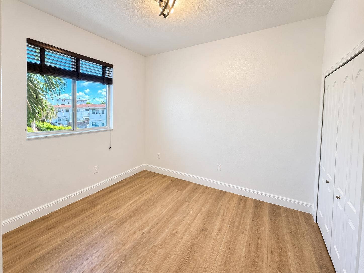 Wood-finish flooring, white walls, and a window with dark wood blinds. Virtually staged.