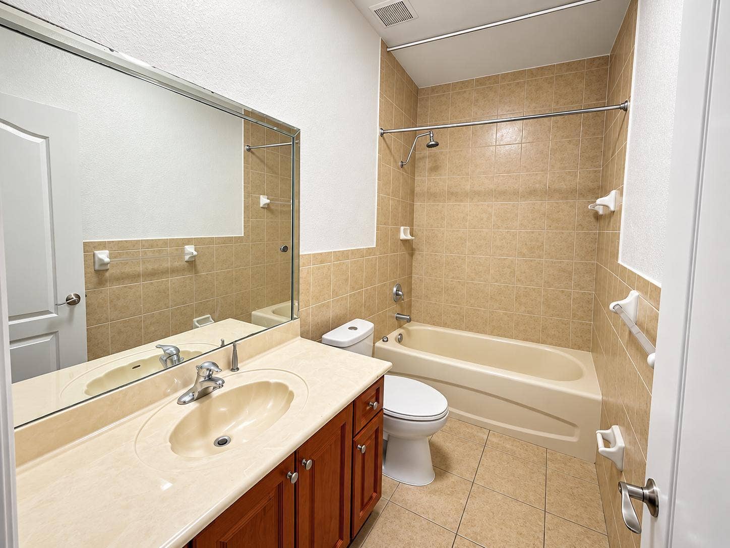 Bathroom featuring a wood-finish vanity with an integrated sink and a large wall-mounted mirror. Virtually staged.
