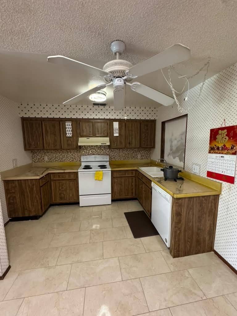 Kissimmee, FL 34744 U-shaped kitchen featuring wood-finish cabinetry, a white electric range, white dishwasher, and light-toned floor tiling